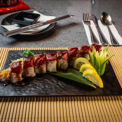 Plate of sushi rolls topped with seared steak and eel sauce accompanied by wasabi and lemon slices.