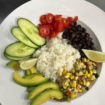 A plate of rice surrounded by corn salsa, avocado, tomatoes, and cucumbers.