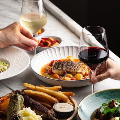 Two people enjoying glasses of white and red wine at a table with served food