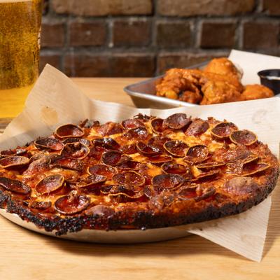Pepperoni pizza, wing plate, and a glass of beer on the table.