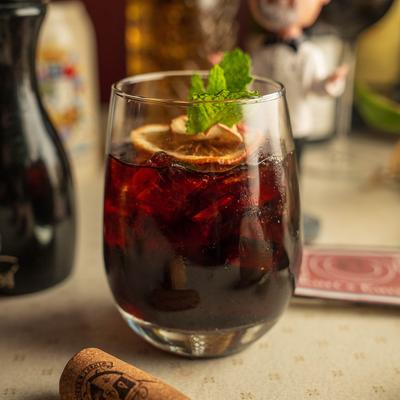 A glass of red sangria garnished with a dry citrus wheel and mint.