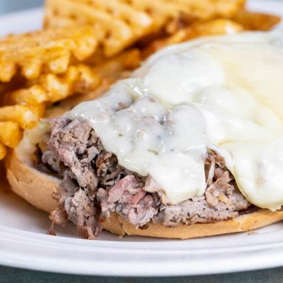 Cheesesteak sandwich served with waffle fries, close-up.