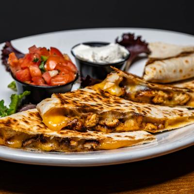 A serving of chicken quesadilla served with pico de gallo and sour cream.