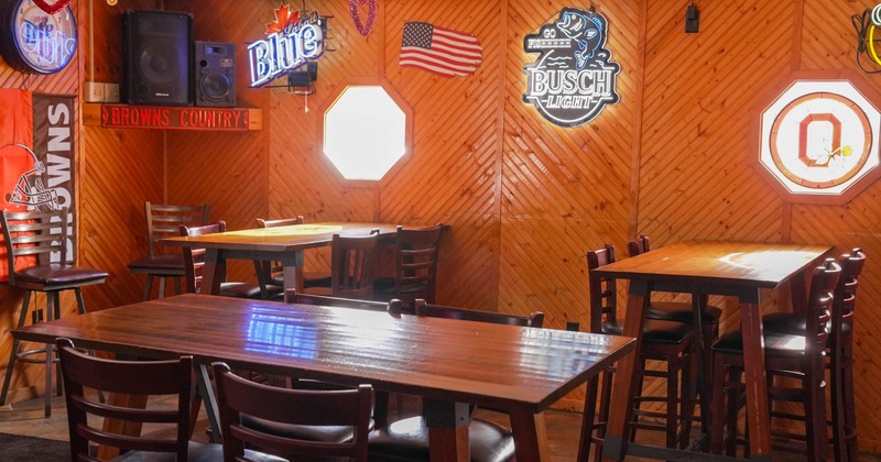 Wood-paneled bar interior with tables, chairs, neon beer signs, sports decor