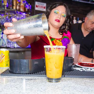 Bartender pours an orange cocktail into a salted-rim glass.