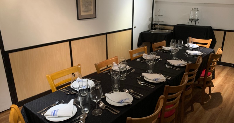 Interior, a long table covered with a dark tablecloth, with place settings and chairs
