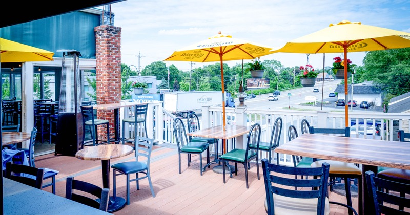 Outdoor dining area with tables, chairs, yellow umbrellas, and a road in the background