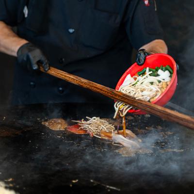 A chef cooking a noodle dish on a large circular griddle.