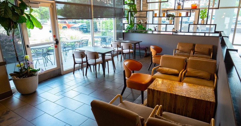 A cozy café interior featuring a glass door, elegant chandelier, beige armchairs, wooden tables