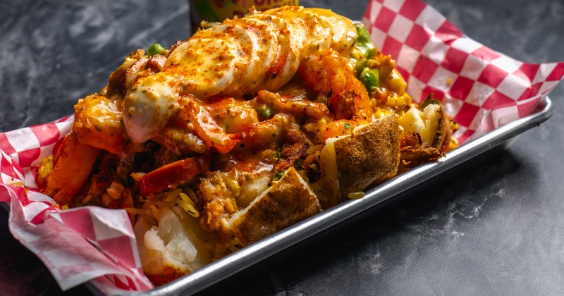 Baked potato with rice, garlic butter, corn, egg, sausage, onions, peppers, shrimp, and crab