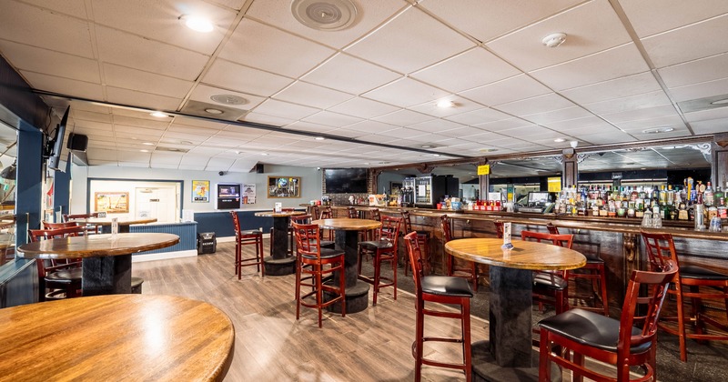 Interior of a bar with wooden tables, stools, and a long counter lined with bottles