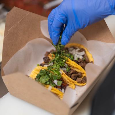 Tacos are being topped with fresh cilantro and diced onion.