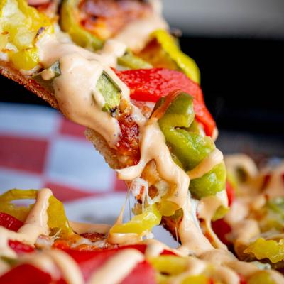 Slice of pizza topped with red and green peppers and drizzled with a creamy sauce.