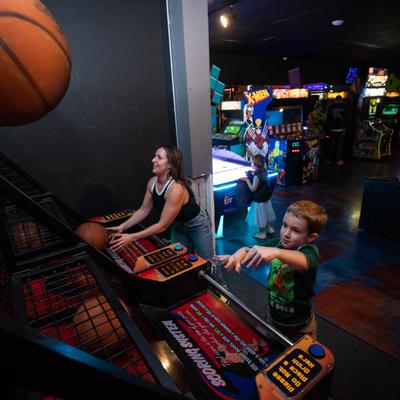 Two guests play an arcade basketball game, arcade machines in the background.
