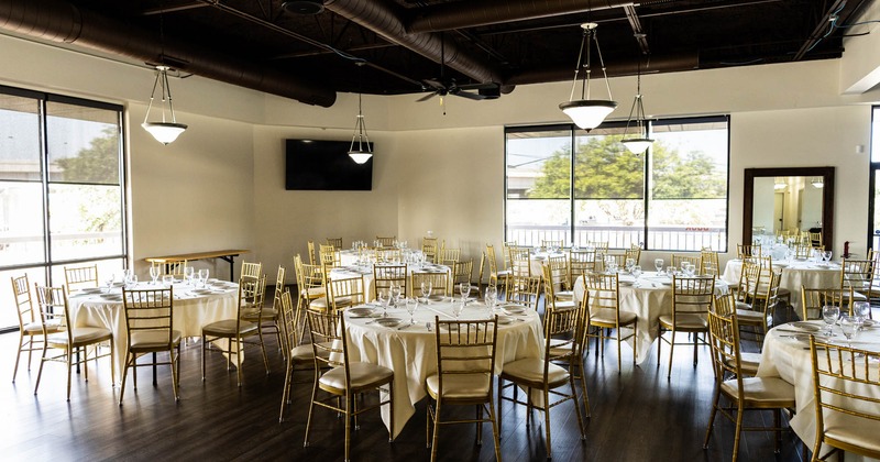 A banquet room with round tables, white tablecloths, and gold chairs set for an event