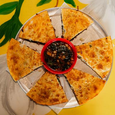Crispy, cheesy birria pizza slices arranged around a savory broth dipping sauce.