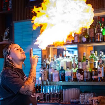 Bartender performing a fire breathing trick with a backdrop of liquor bottles.