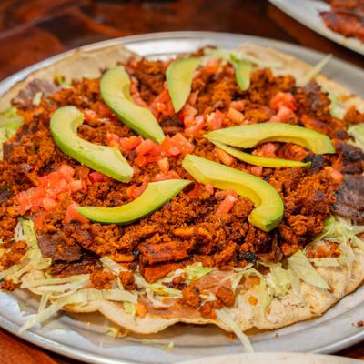 Corn tortilla topped with steak, chorizo, beans, lettuce, tomatoes, avocado, and cheese.
