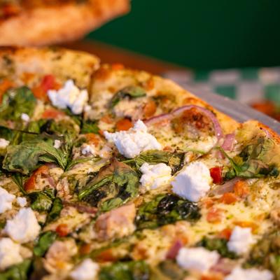 Pesto Supremo Pizza topped with spinach and ricotta, close-up.