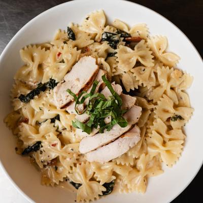 Bowtie pasta in creamy sauce topped with sliced chicken and fresh basil.