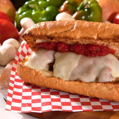 Meatball sub sandwich with melted cheese, fresh vegetables in the background.