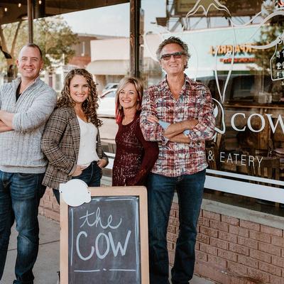 Group portrait of the owners standing by The Cow board sign in front of the restaurant