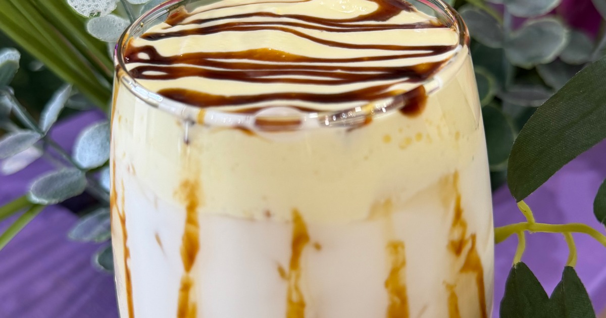 Creamy layered drink with frothy yellow foam and dark chocolate syrup drizzle