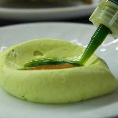 Close-up of green mousse with amber sauce and green liquid being added on a white plate.