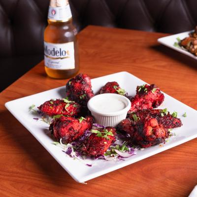 Tandoori chicken wingsc and a dip, beside bottle of beer.