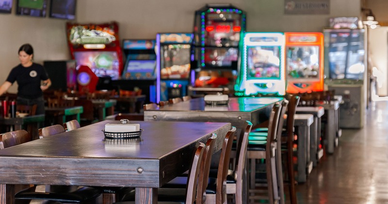 Interior, seating area, closeup of lined up tables, arcade games in the background
