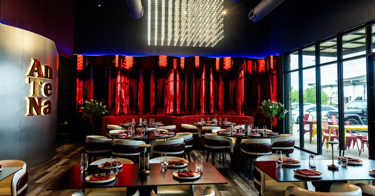Modern interior with red and metallic accents, featuring a chandelier and large windows.