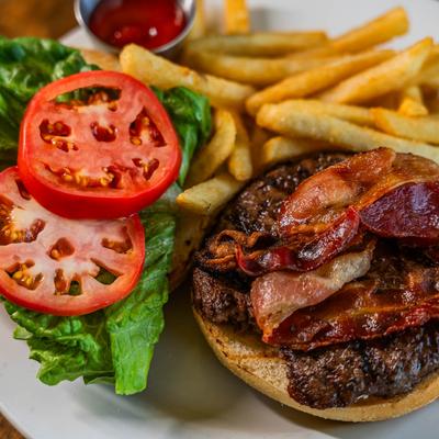 Close up of a burger with bacon, tomato, and lettuce, served with fries and ketchup.