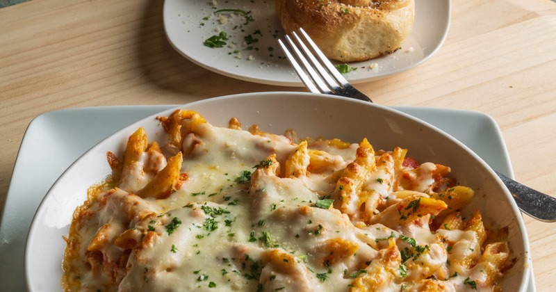 A plate of baked ziti served with two garlic knots on the side