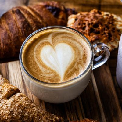 A cup of latte sits on a wooden table, surrounded by pastries.