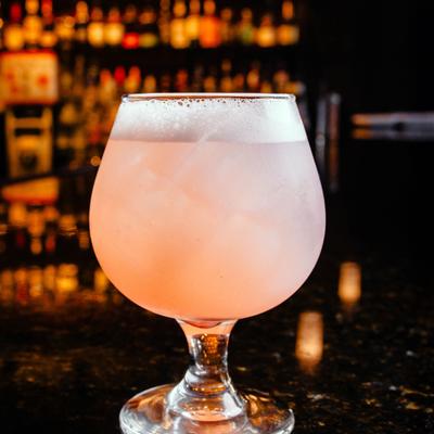 A frosty, pink Lychee Martini cocktail in a round glass sits on a dark, reflective bar top.