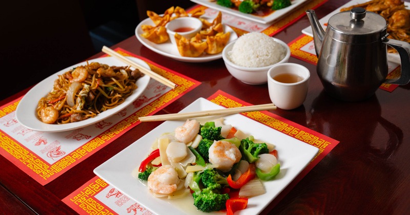 Chinese food spread with shrimp and scallop stir-fry, noodle dish, fried wontons, and rice
