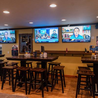 Sports bar interior with high tables, stools, and multiple TVs on the wall.