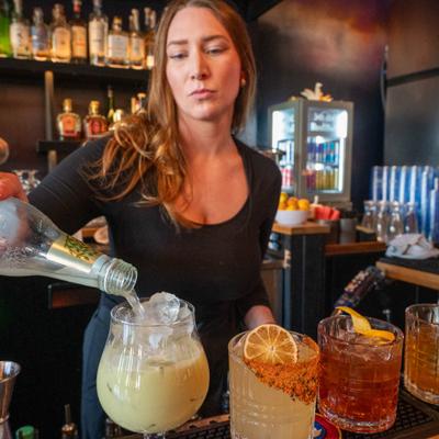 Bartender preparing multiple cocktails on a bar conter.