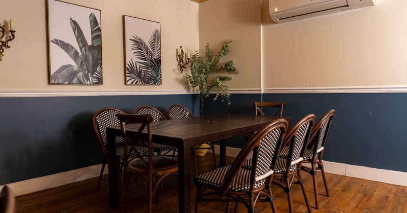 Dining room with a dark wooden table, bistro-style chairs, and tropical leaf prints on the wall