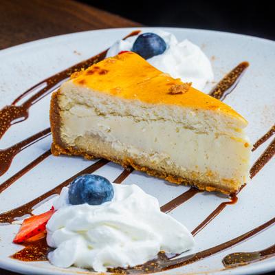 Cheesecake slice with whipped cream, berries, and chocolate drizzle.