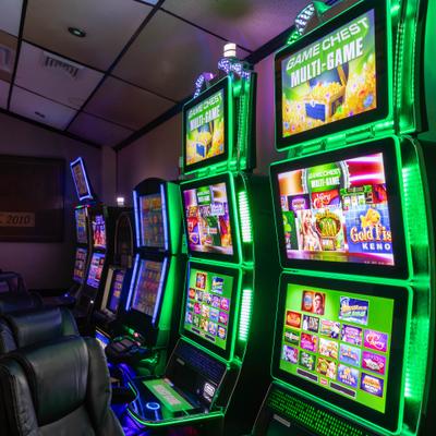 Row of green lit slot machines in gaming area.