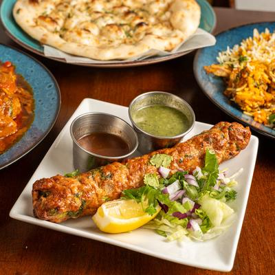 A plate of Chicken Seekh Kabab served with chutneys, surrounded by assorted dishes.