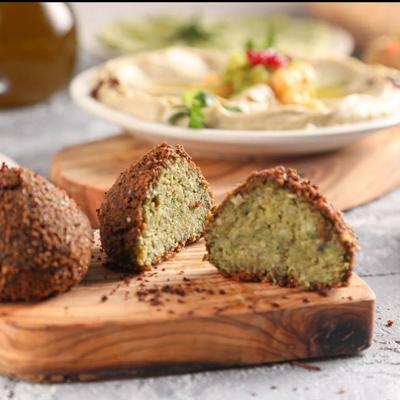 Close-up of two pieces of falafel, one cut open to show the green interior, on a wooden board.