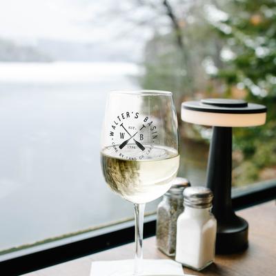 A glass of white wine on a table with a scenic lake view in the background.