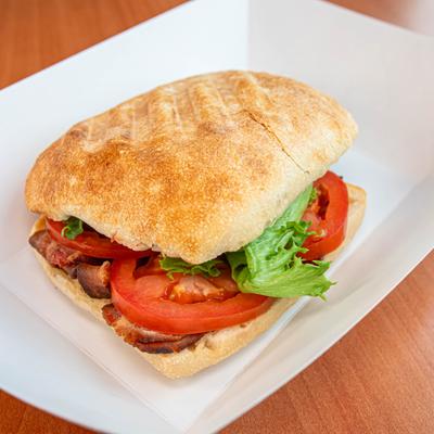 Sandwich with bacon, tomatoes, and lettuce on square plate.