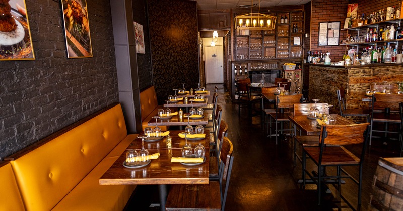A cozy interior - yellow benches and wooden tables, a bar area on the right, art on dark brick walls