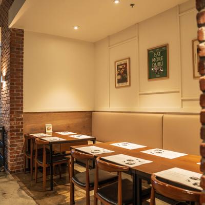Booth dining area with wooden tables, brick walls and framed ar.