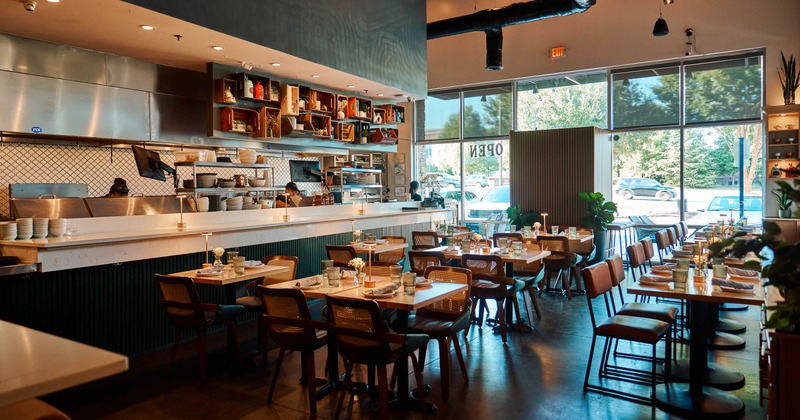 Interior with an open kitchen, neatly set dining tables, large windows
