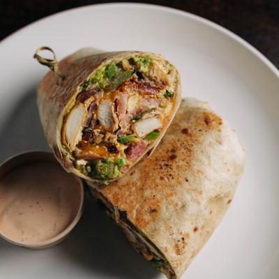 A grilled chicken burrito served with a side of dipping sauce.