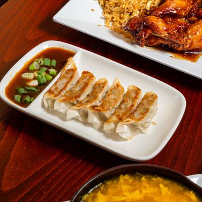 Pan fried dumplings with dipping sauce, served next to wings and soup.